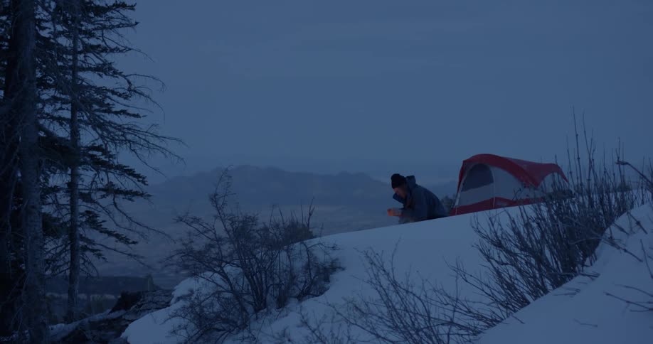 Man sitting in front of the campfire warms his hands on the snow covered hill