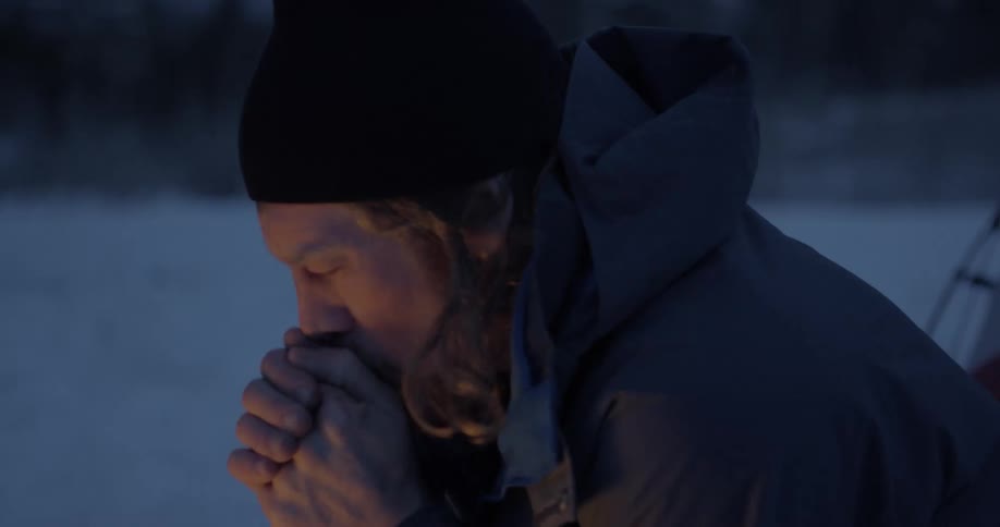Man makes a fire and warms his hands on the snow covered field