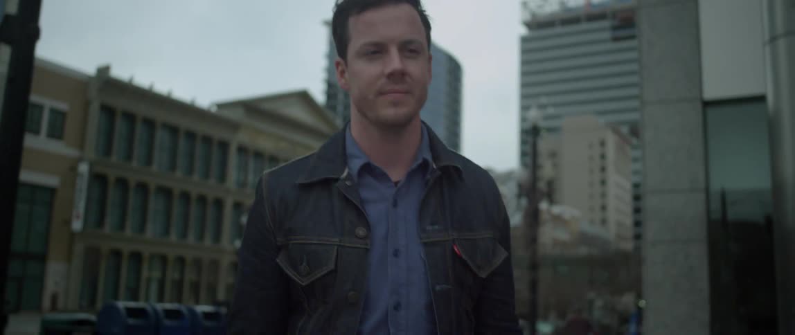 A man in a jean jacket walks in a city