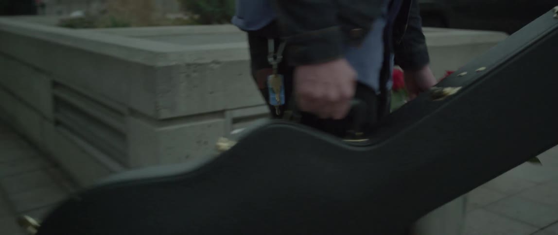 A man carries a bucket of roses and a guitar case on a city sidewalk