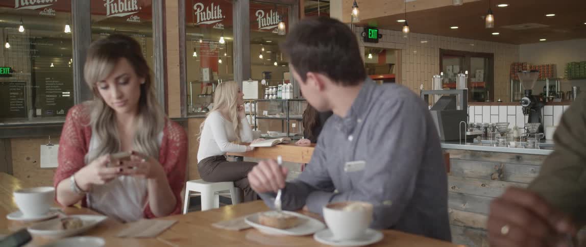 People are sitting in a restaurant eating reading and using a phone