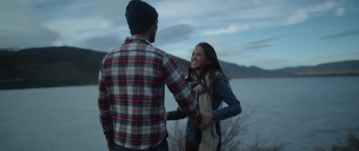 A man twirls a woman romantically near a lake on a chilly fall evening