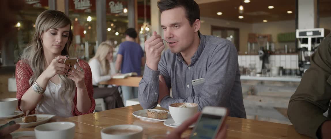 A man eats while others at the table look at their cell phones
