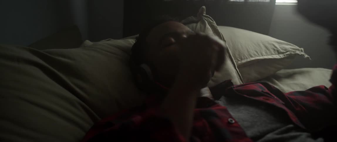 A man lying in bed puts on headphones and closes his eyes