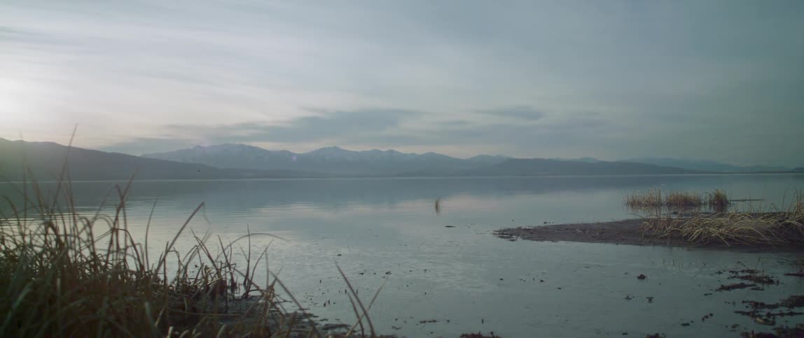 A large lake has a snow covered mountain in the distance
