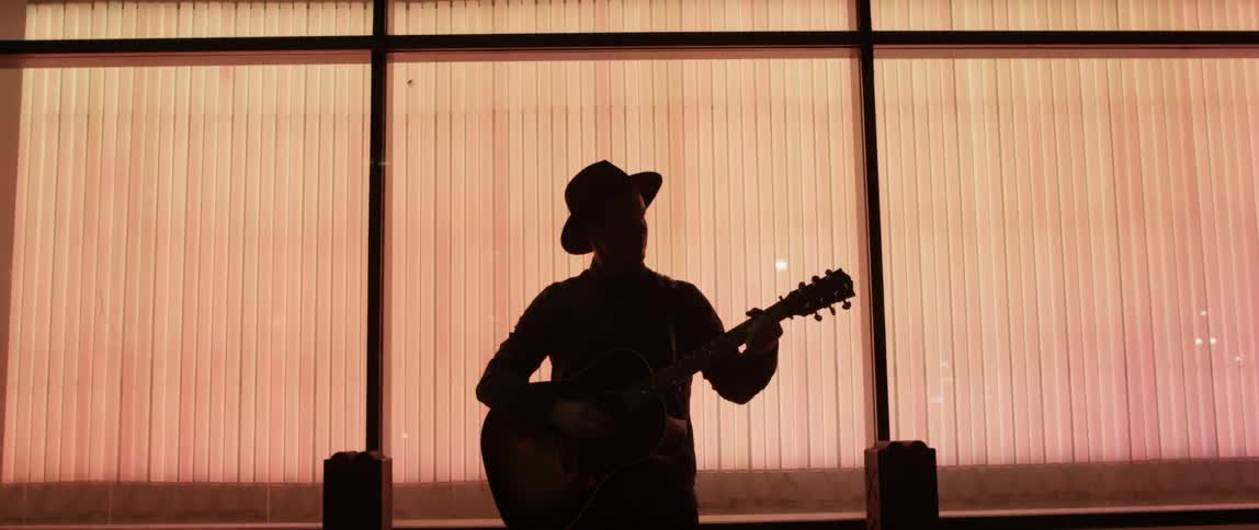A man is playing a guitar in front of a large window