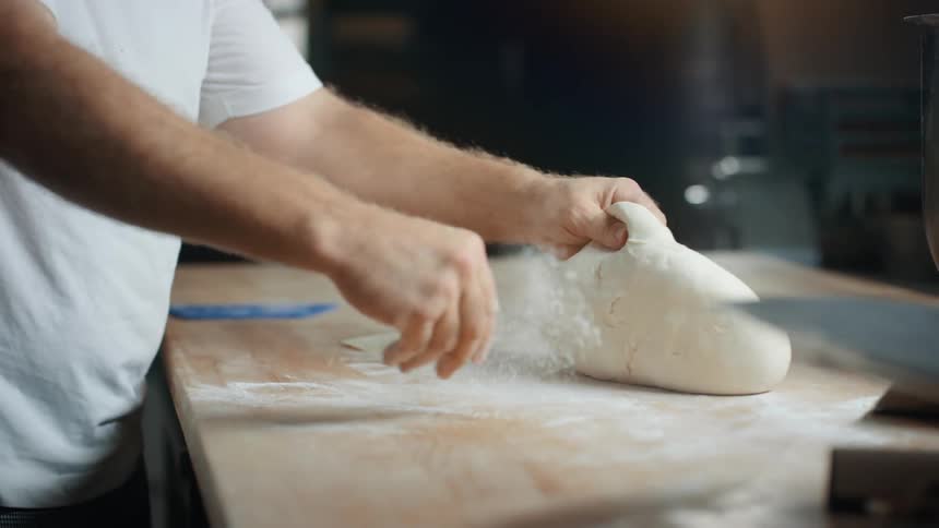 A man sprinkling flour on a table underneath dough