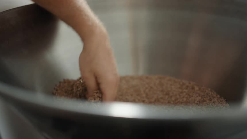 Man stirs the grain with his hand in a large silver bowl