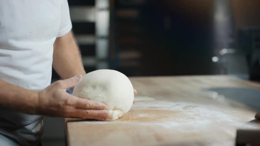 A male rolling out dough on a counter