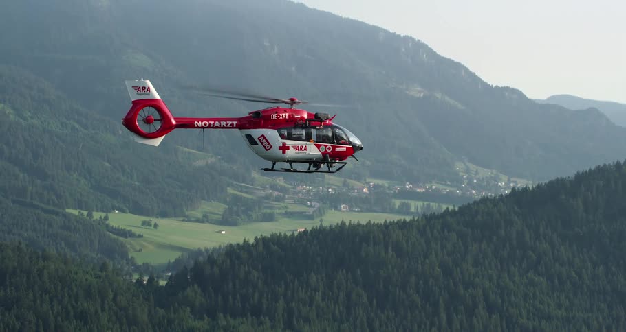 A medic helicopter flies over a mountain with dense tree cover