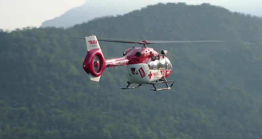 A helicopter flying over a forest with mountains in the background