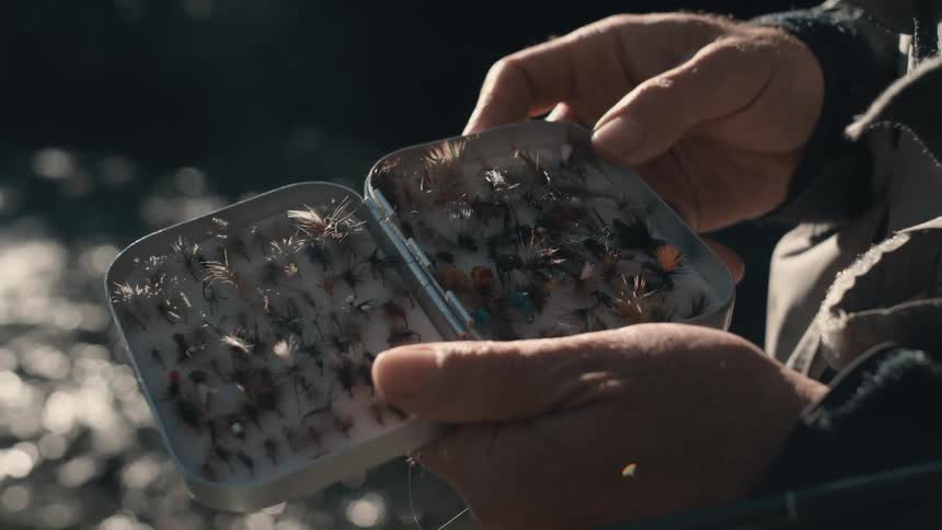 Close up of hands opening a tin container to organized fly fishing lures