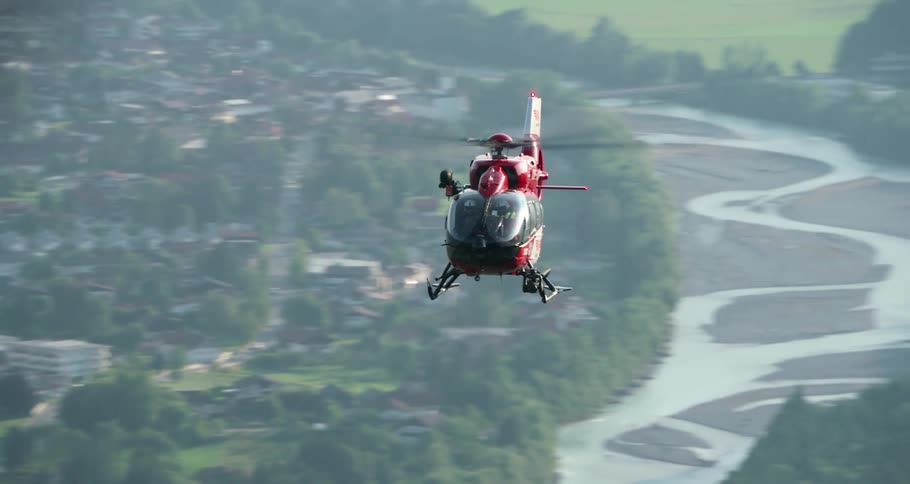 A red helicopter flying over river and neighborhood