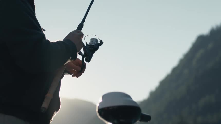 A man fishes while standing in a boat on a sunny day
