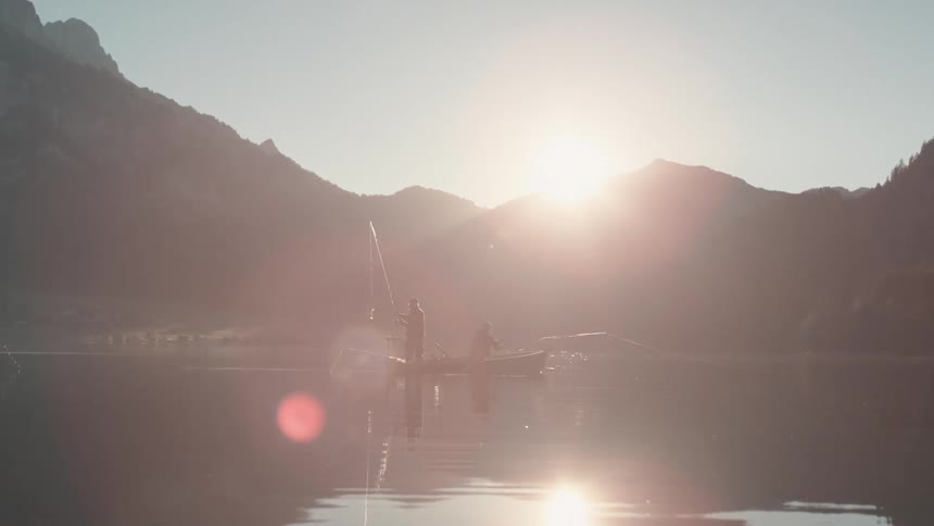 Two people stand in a boat fishing on a lake
