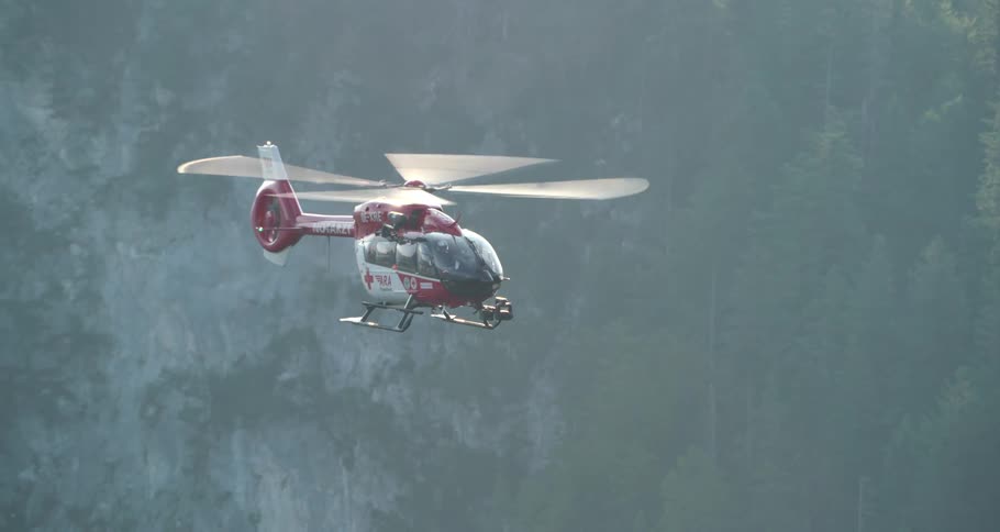 Helicopter with red medical cross flies over mountain forest during foggy day