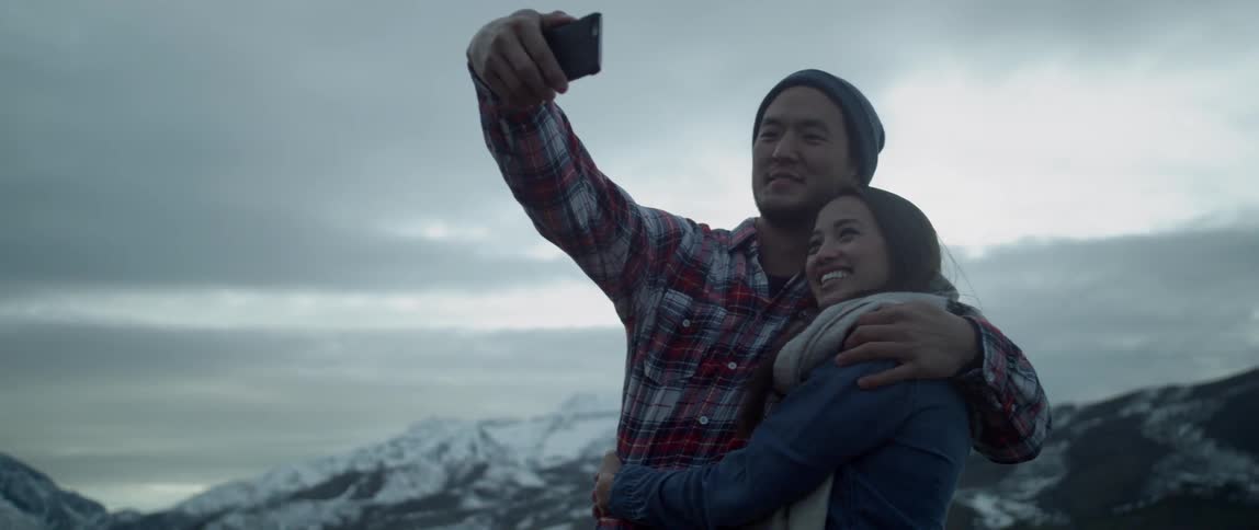 A couple take pictures on a mountain on a cloudy day