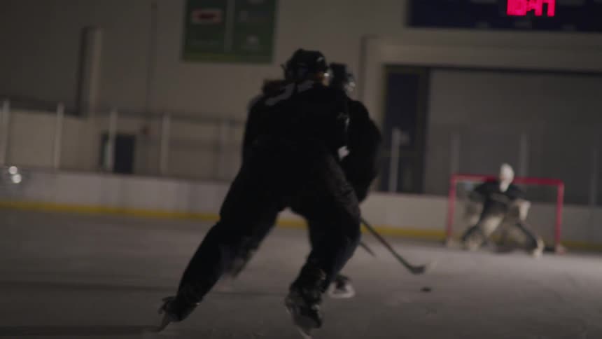 A goalie guards the net as a player prepares to shoot the puck