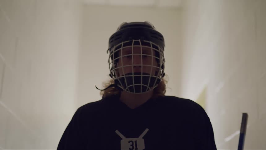 A person in hockey equipment standing in a narrow white brick hallway