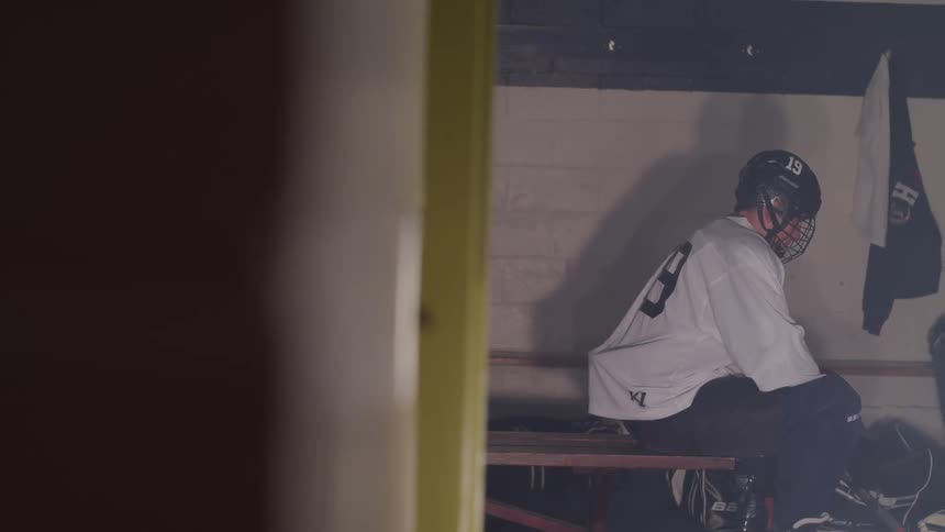 A hockey player sits on a bench by himself in full gear