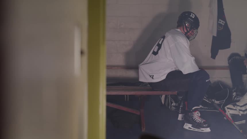 A hockey player in uniform sits on a bench in a concrete building
