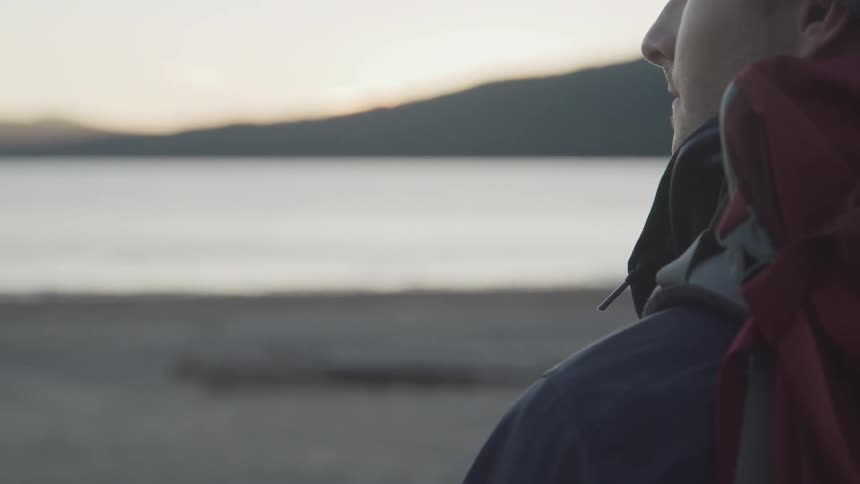 A man with a backpack stands and looks out at the water