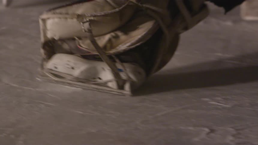 A hockey player shoots a puck at a net as a goalie tries to stop it