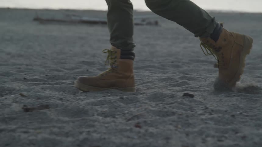 Man walking at the sand on the beach wearing boots and jeans