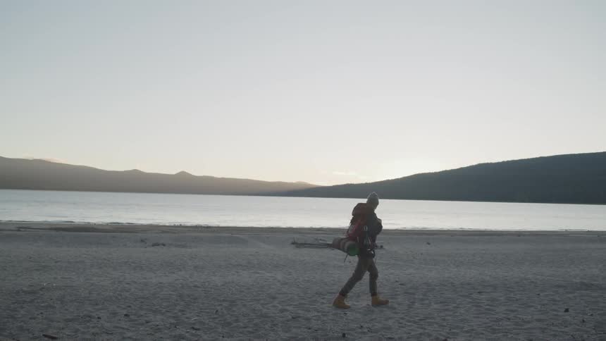 A teenager hiking walks across a beach