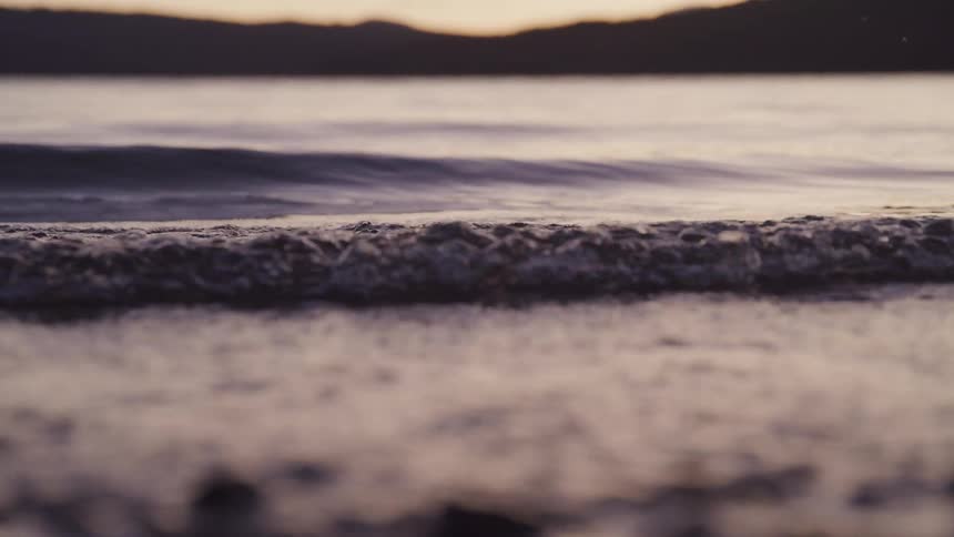 Small waves break against the shore at dusk