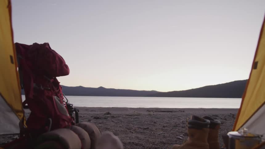 A camper crossing their legs while relaxing in a tent on the shore of a lake