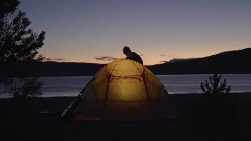 A man walks to his lake side tent at night