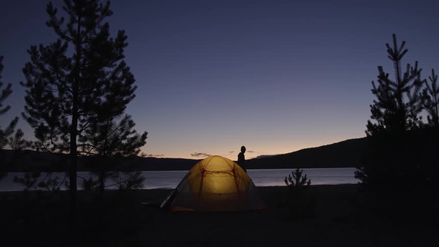 A camper walking in front of their tent at a lakeside at sunrise