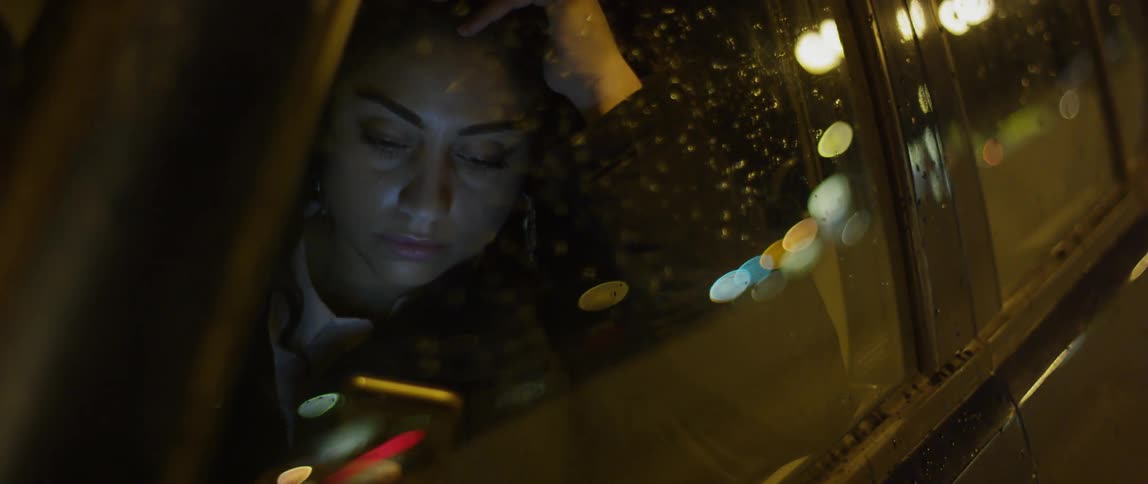 A woman plays on a smartphone while sitting in a vehicle at night
