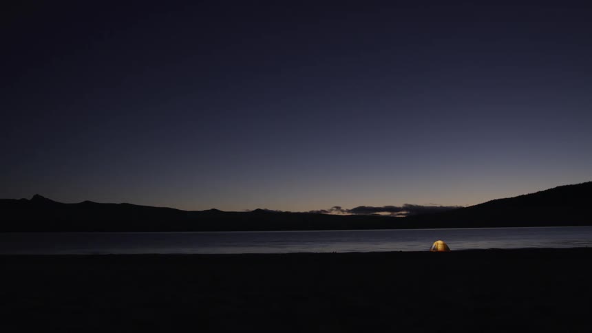 The sun starts to rise over a lake where a single tent is the only sign of life