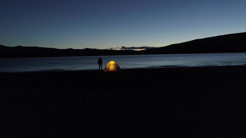 Man standing in front of a lake next to his yellow camping tent contemplating the landscape