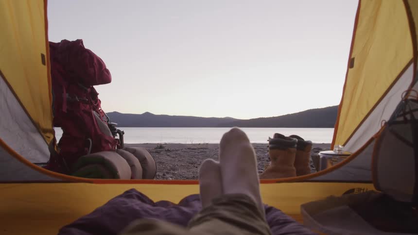 A person lays in a tent beside a lake