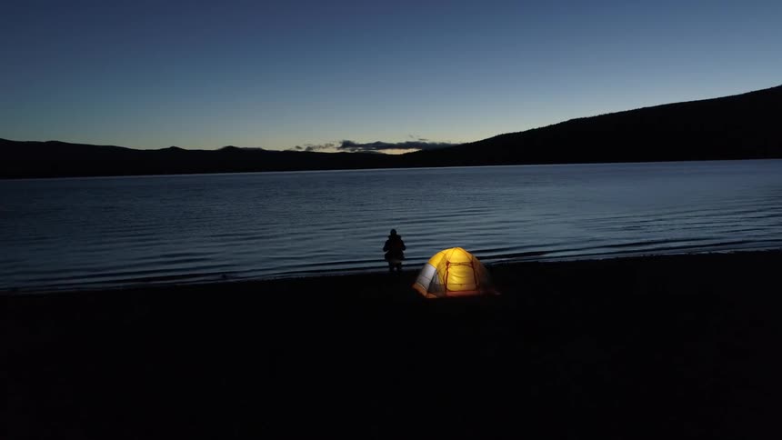 A person walks from a tent toward a lake at night