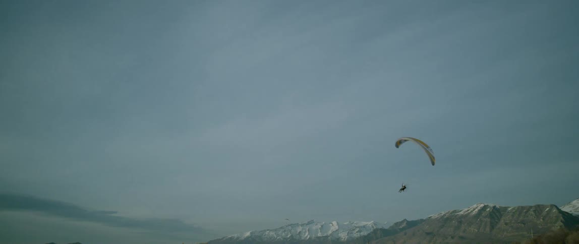 A person with a yellow parachute glides over a mountain