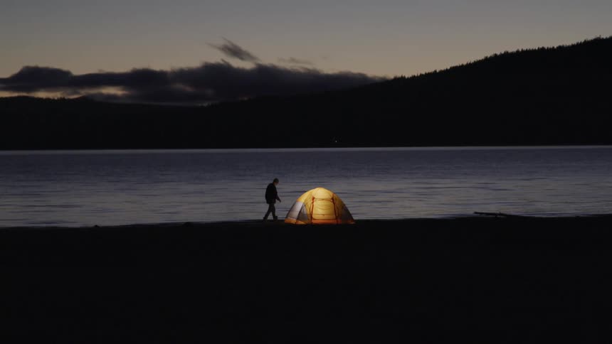 Man walking towards his yellow camping tent next to a lake