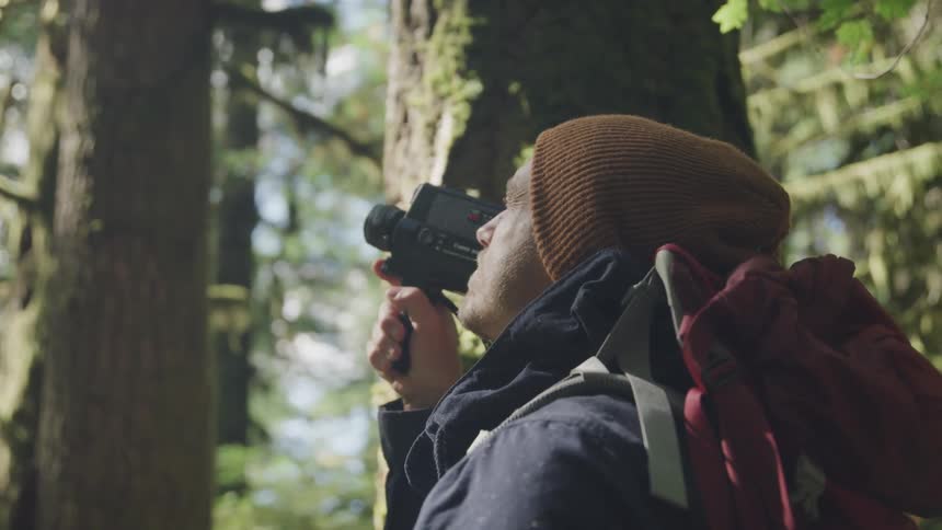 Man adjusting lenses on older video camera then filming in a forest