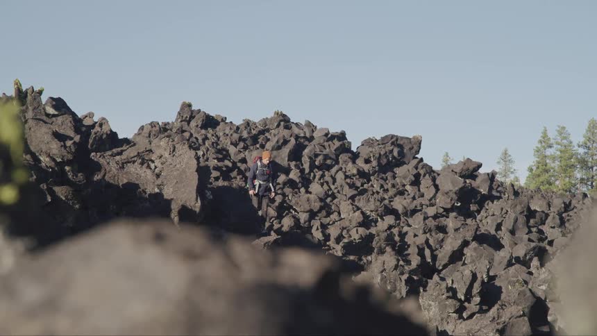 A person hiking on black rocks with trees and the sky in the background