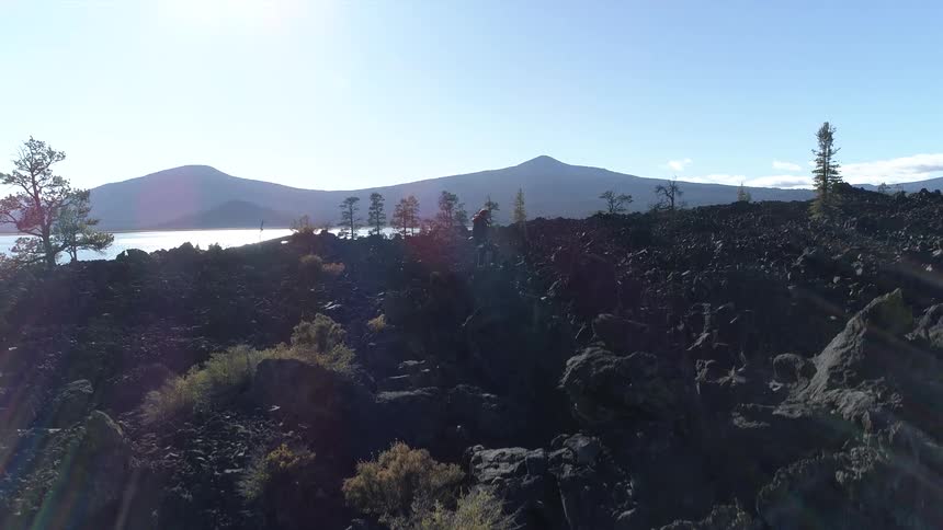 A hiker stands in profile on a rocky ridge with hills and lake behind