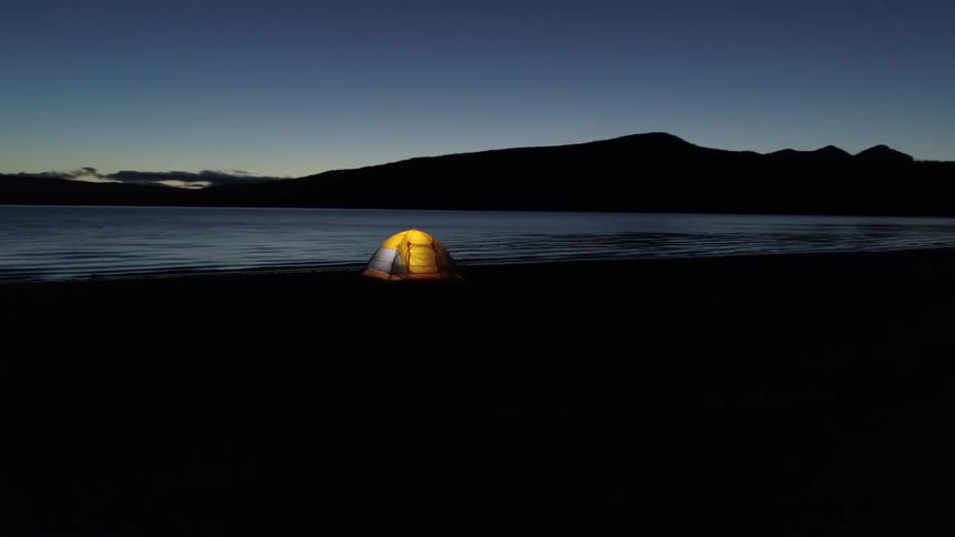 A lit up tent sits in front of a peaceful lake