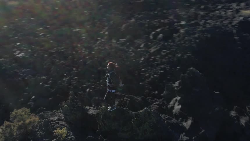 A man stands on top of a large rock pile surrounded by a tree lined forest