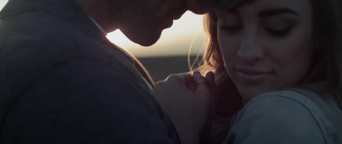 A man and woman are holding each other as the sun sets