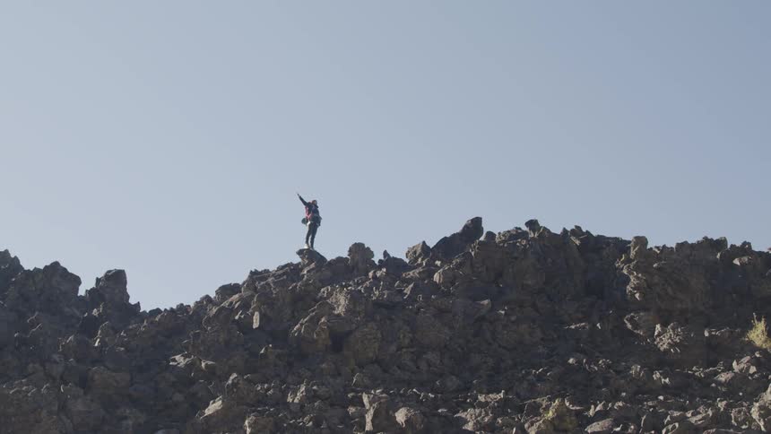 Person standing at the top of rocks and opening up his arms