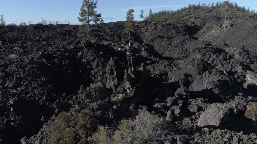 A teenager out hiking stands on a large rock with his arms spread out to his sides