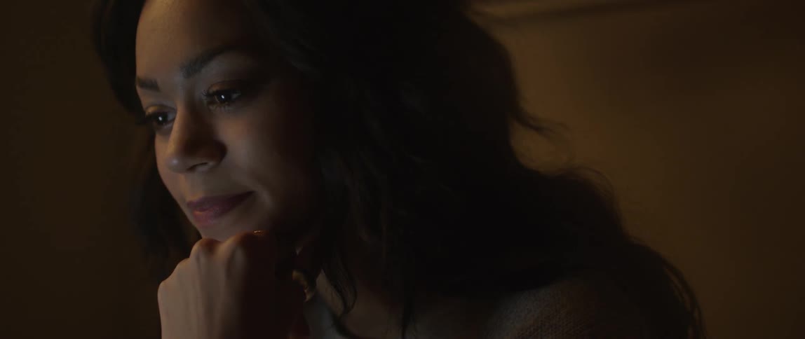 A woman puts her hand to her chin as she looks down