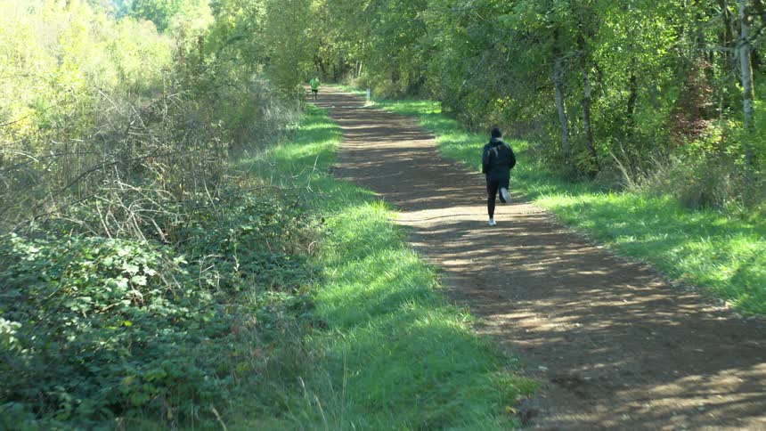 Two men jog on a dirt path on a sunny day